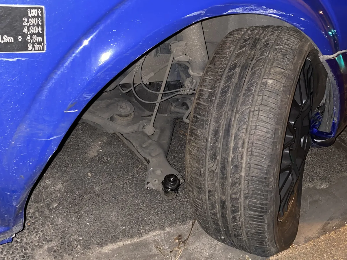 The front wheel of a blue van leaning in at a strange angle after a ball joint failed