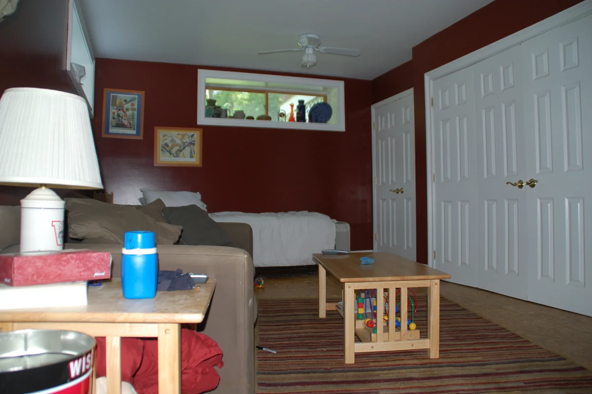 A furnished basement den with a sofa, window, closets and small tables.