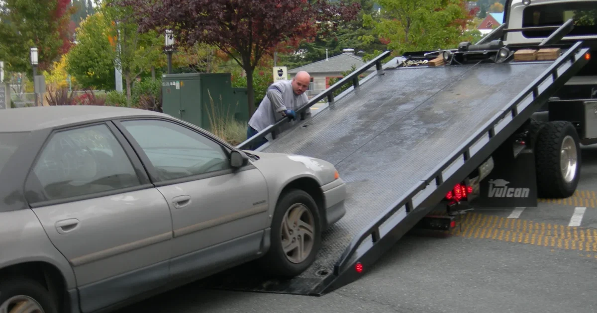 A silver car being pulled up onto a flatbed tow truck