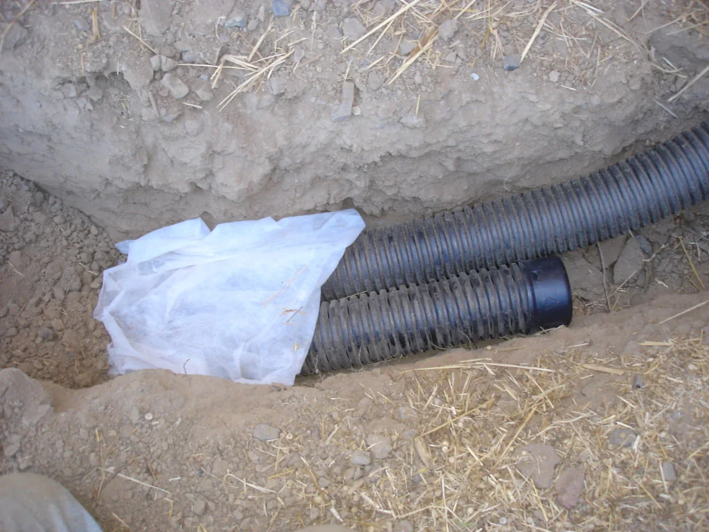 A French-drain trench showing a pipe surrounded by white fabric.