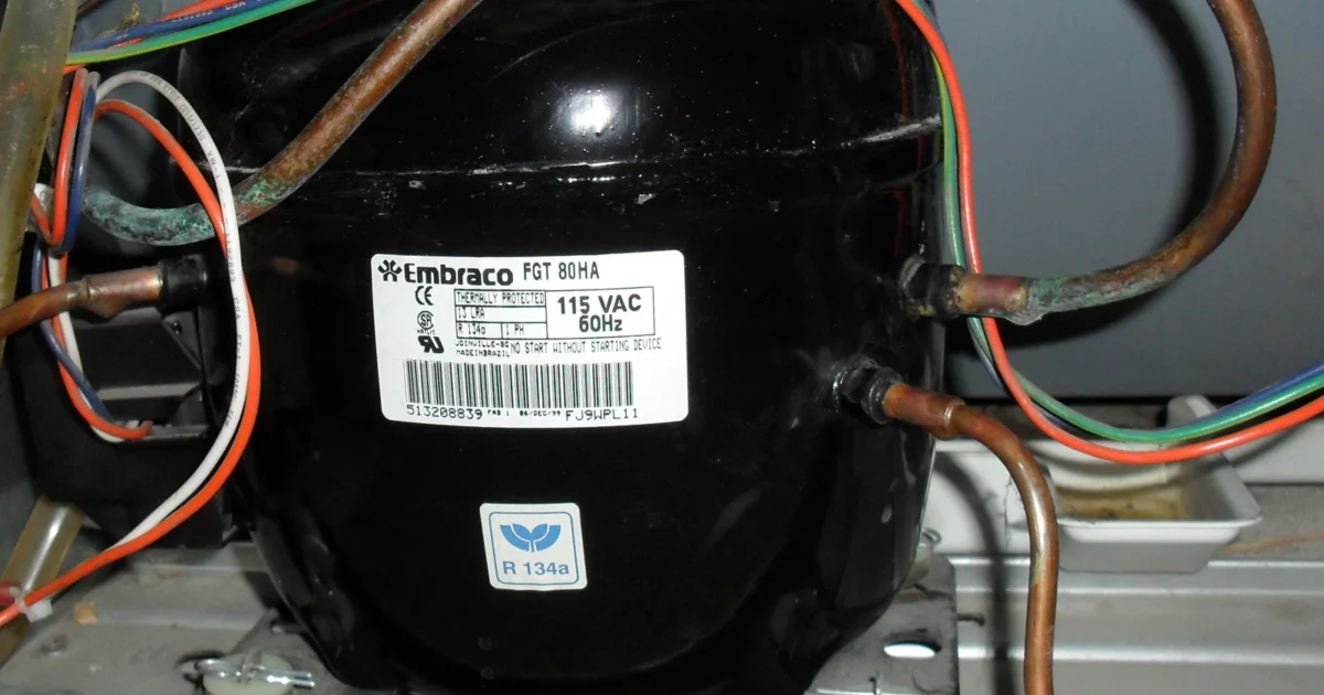 Black refrigerator compressor with copper tubing and electrical connections.
