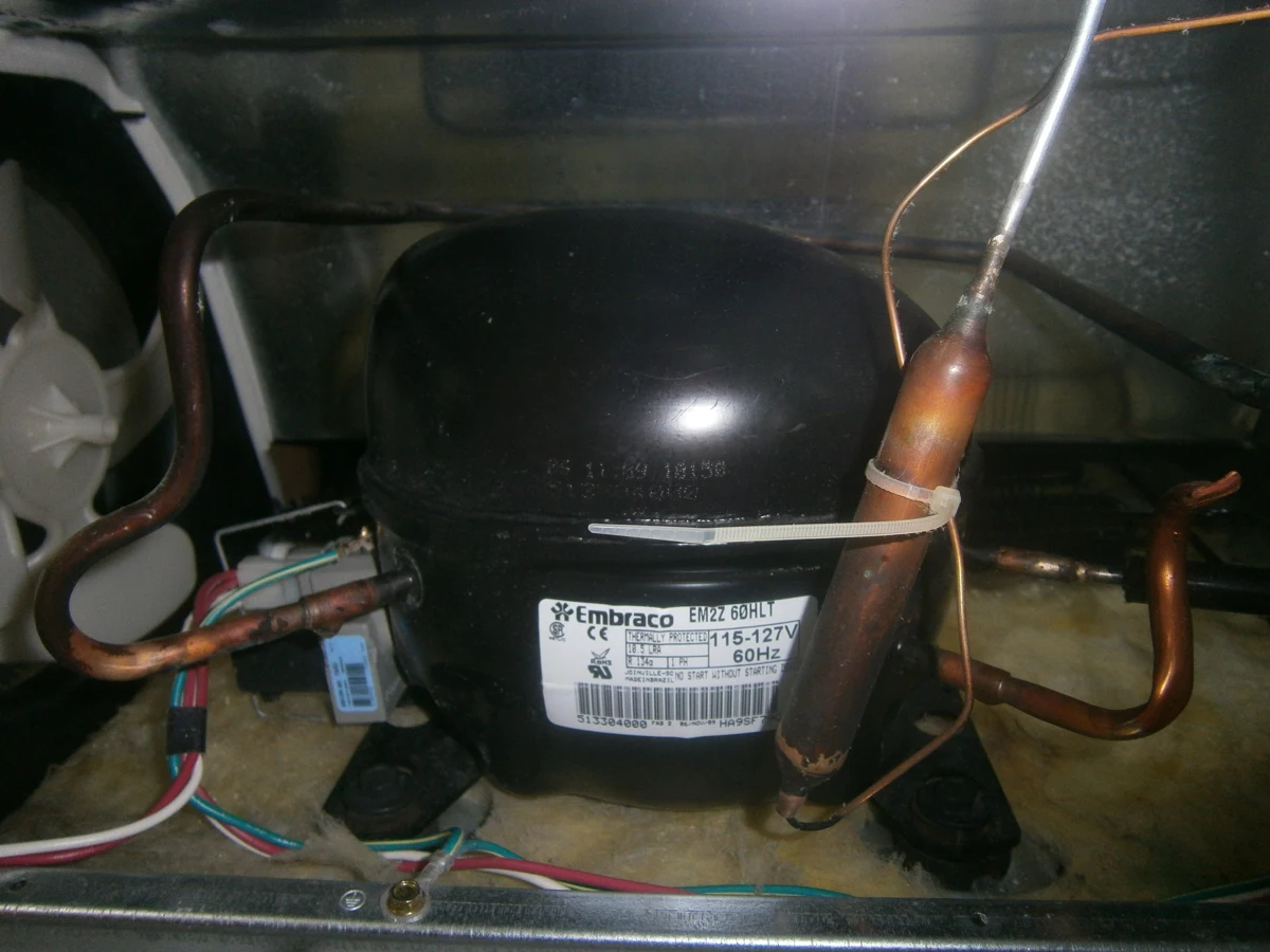 A refrigerator compressor mounted beside its tubing at the rear of the appliance.
