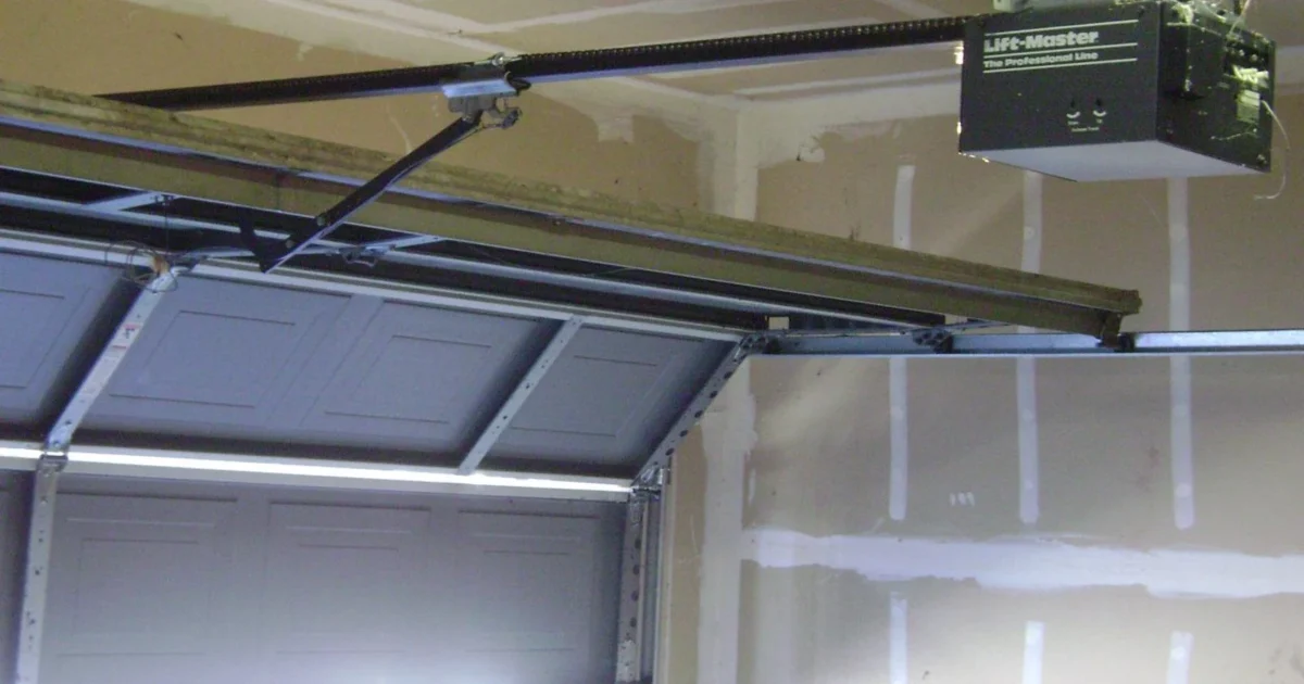 Ceiling-mounted garage door opener and rail above an open sectional door.