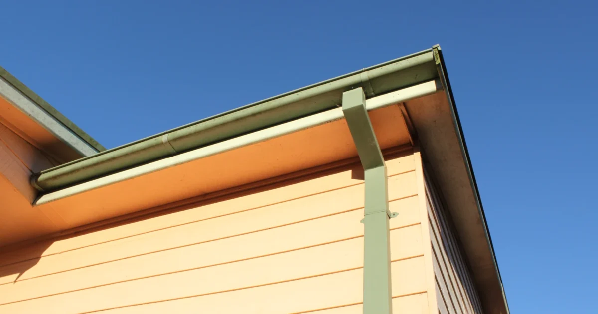 Green gutter and downspout along the roof edge of a house.