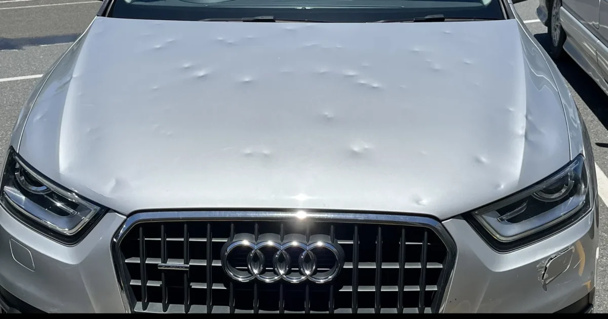 A silver Audi with many small hail dents across its hood