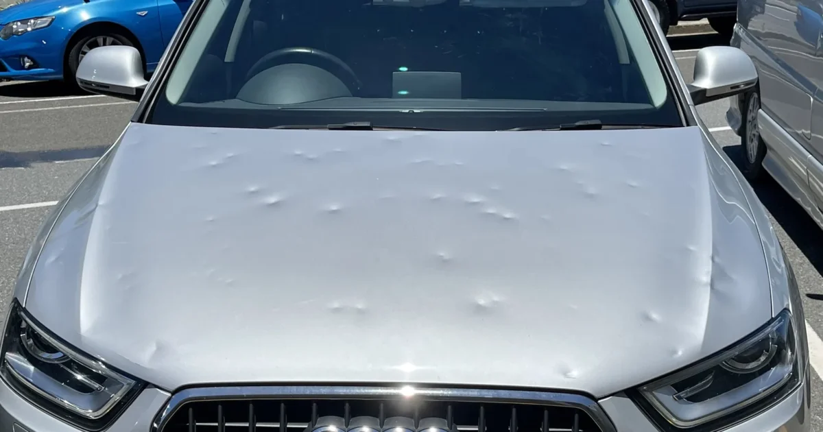 The front of a silver Audi SUV in a parking lot, its hood covered in small round hail dents
