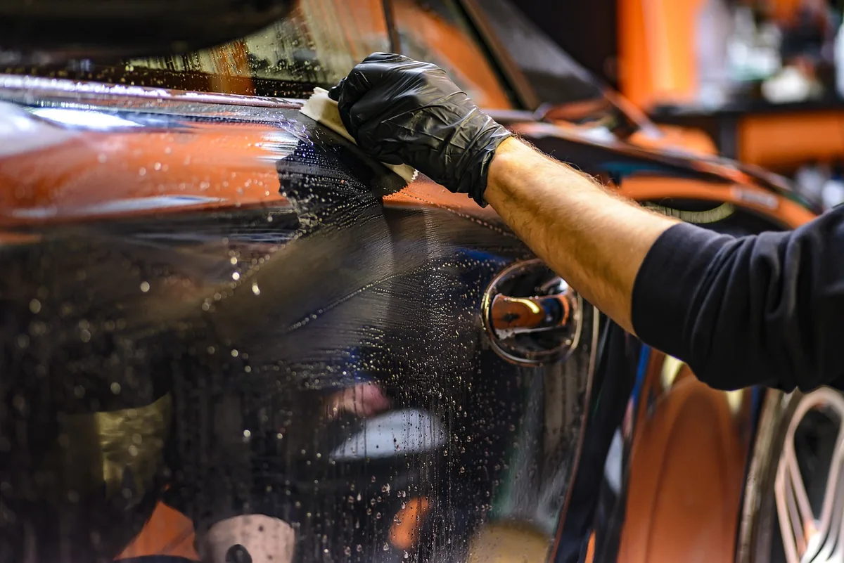 A gloved hand working on a dark car's paint in a detailing shop