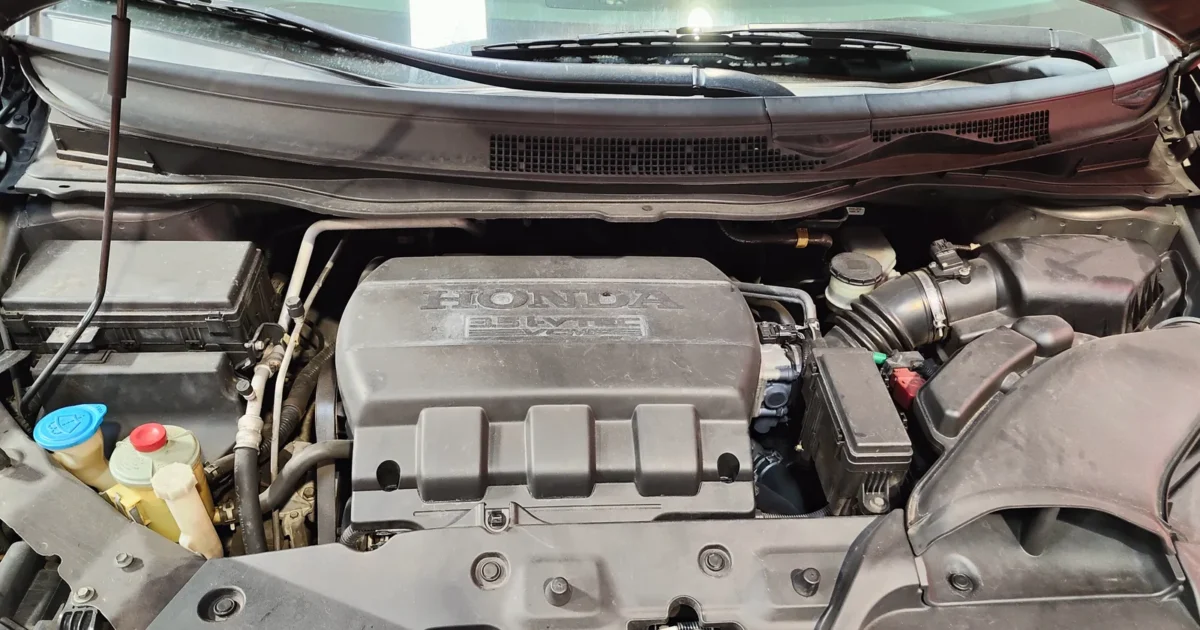 The engine bay of a Honda with its 3.5 liter V6 engine under a black engine cover