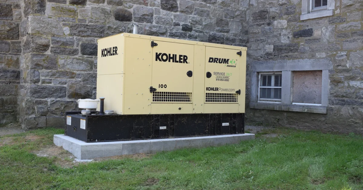 A larger enclosed Kohler backup generator outside a stone building.