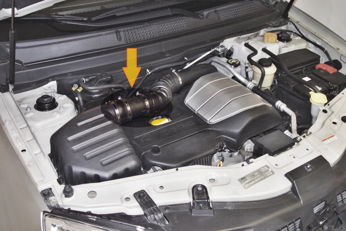 An open engine bay with an orange arrow pointing at the mass air flow sensor in the air intake tube