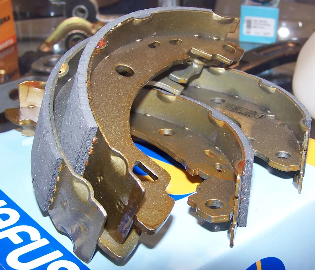 A set of new curved brake shoes with gray friction linings on their metal frames, stacked on a counter