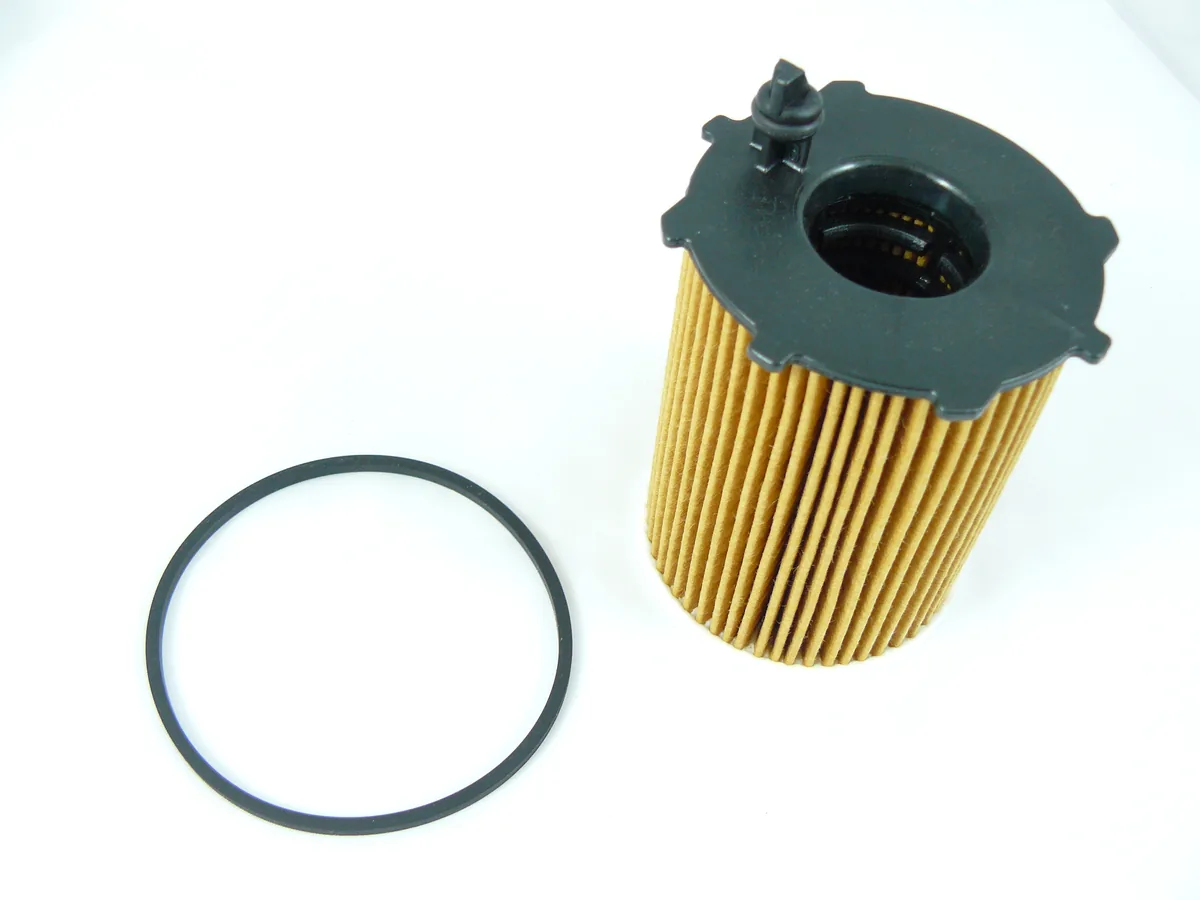 A paper oil filter cartridge with a dark top next to a large black rubber O-ring on a white background
