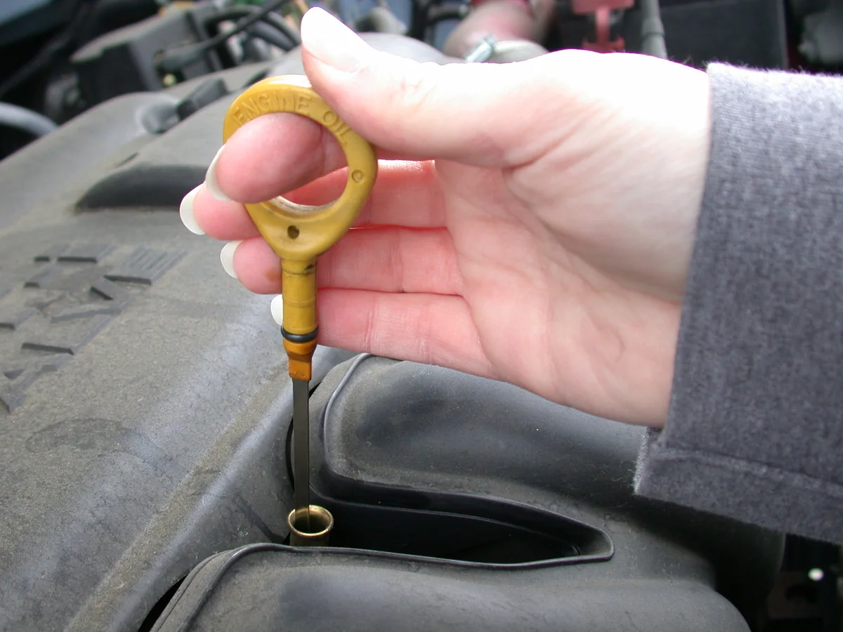 A hand lifting the yellow engine oil dipstick from its tube.
