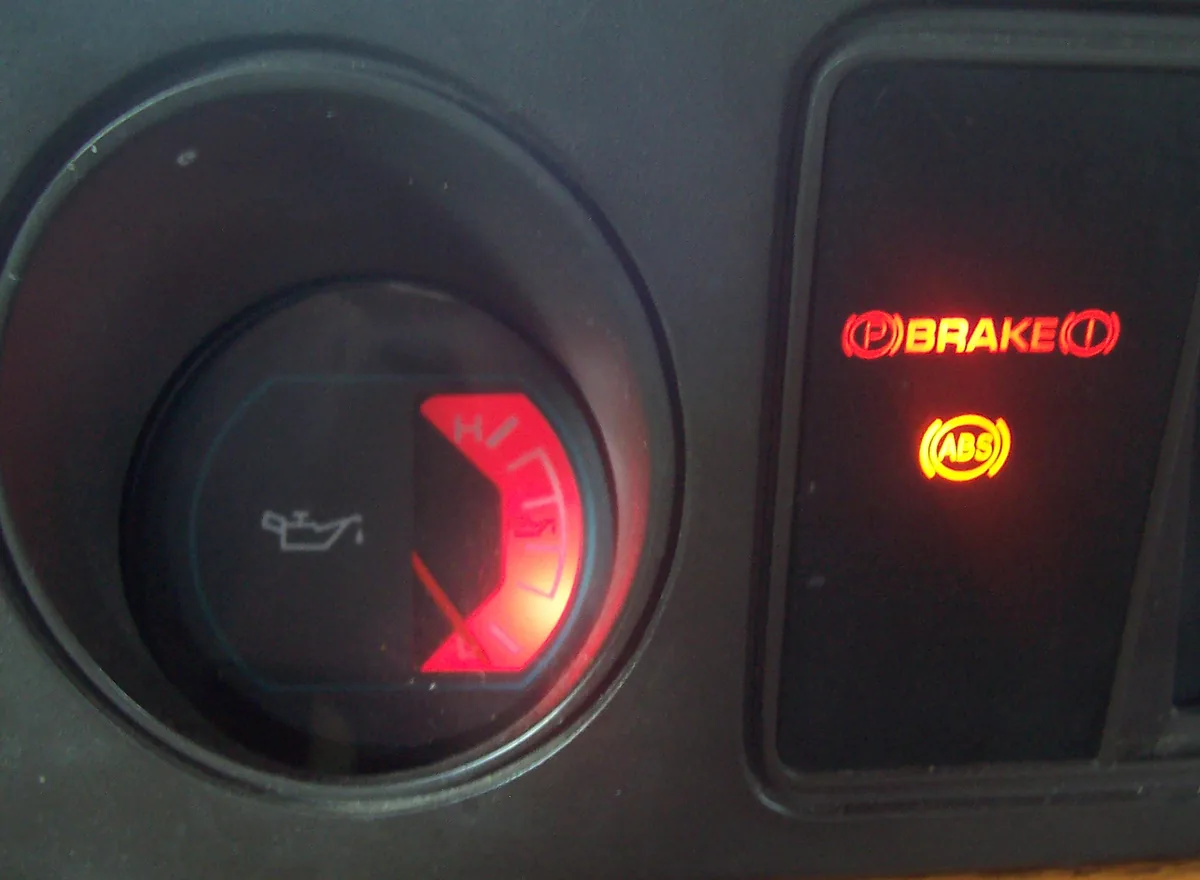 A round dashboard gauge with an oil can symbol glowing red, next to red brake and ABS warning lights