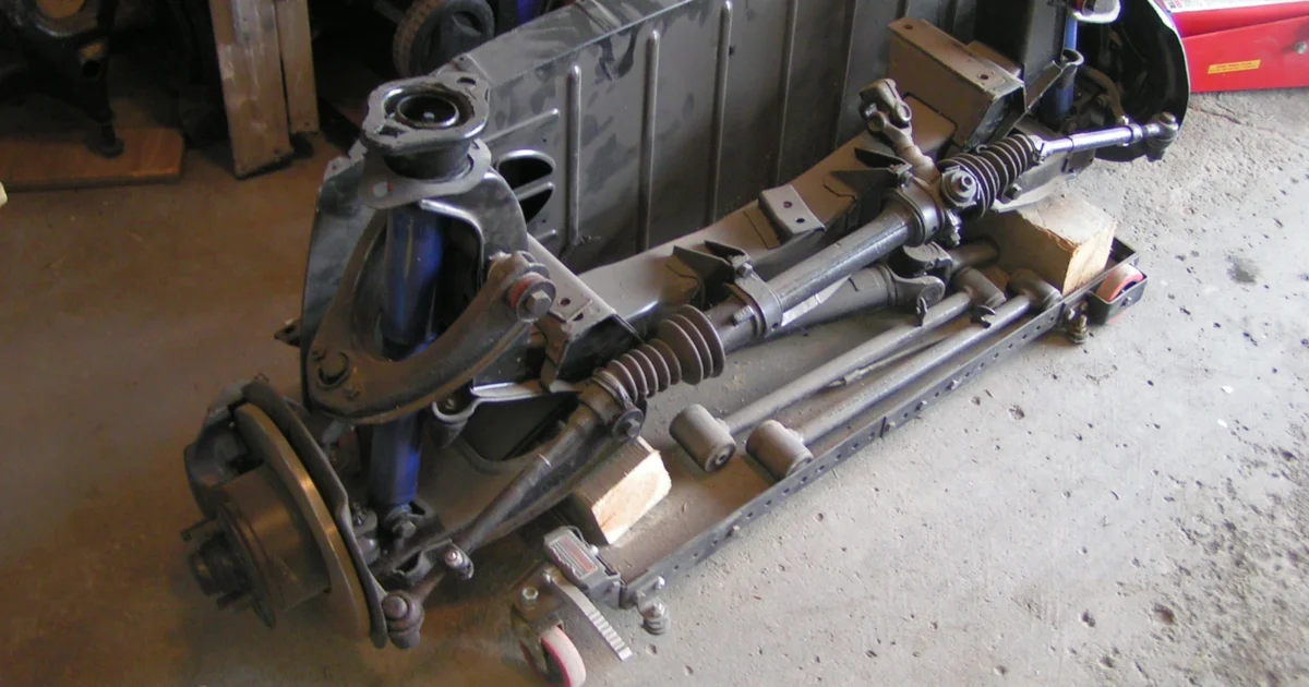 Real reconditioned Opel GT front suspension with steering rack and rubber bellows visible across the assembly.