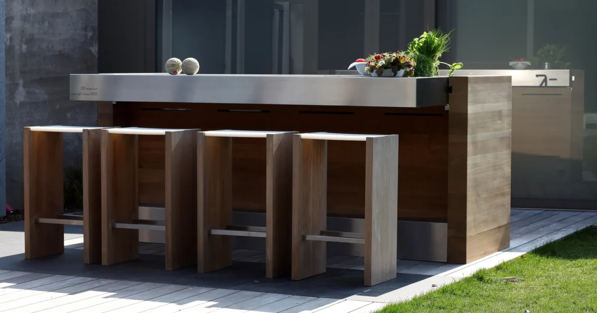 An outdoor kitchen island with a stainless-steel counter and four tall wooden stools.