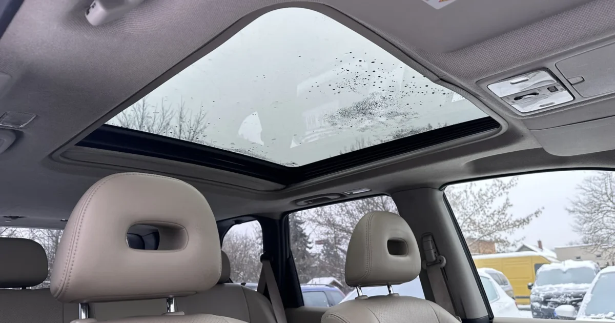 The inside of an SUV with a large panoramic glass sunroof above the front seats, rain drops on the glass