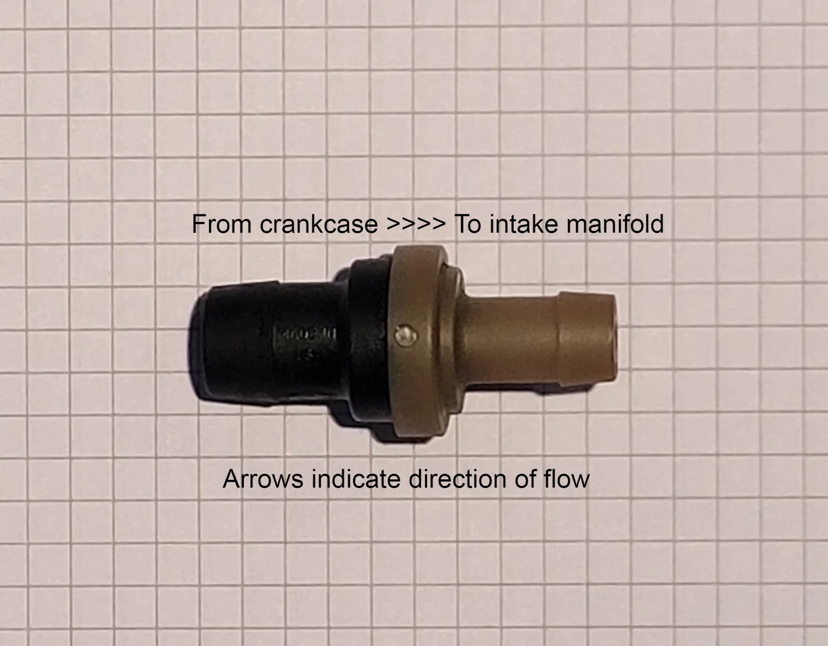 A small black and brass PCV valve on graph paper, labeled from crankcase to intake manifold