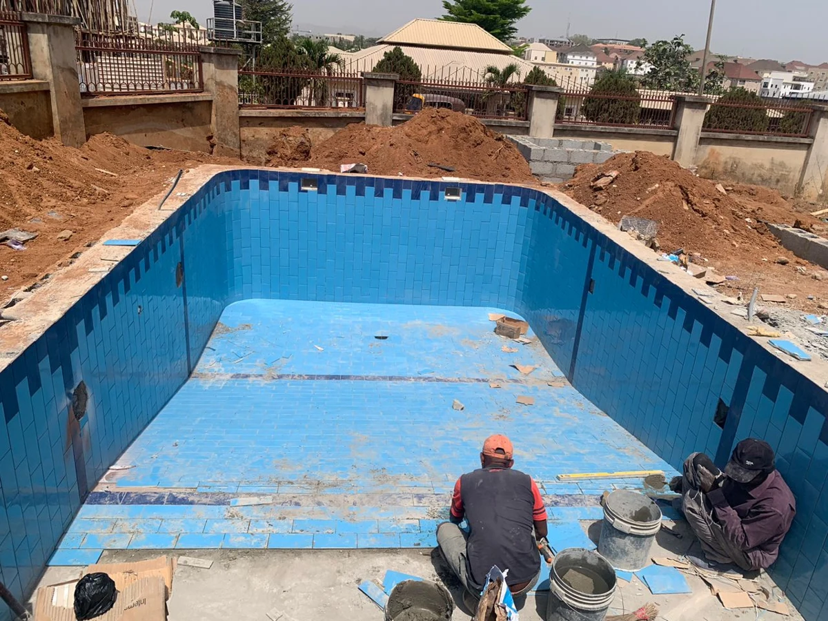 Workers fitting tiles inside an empty swimming pool.