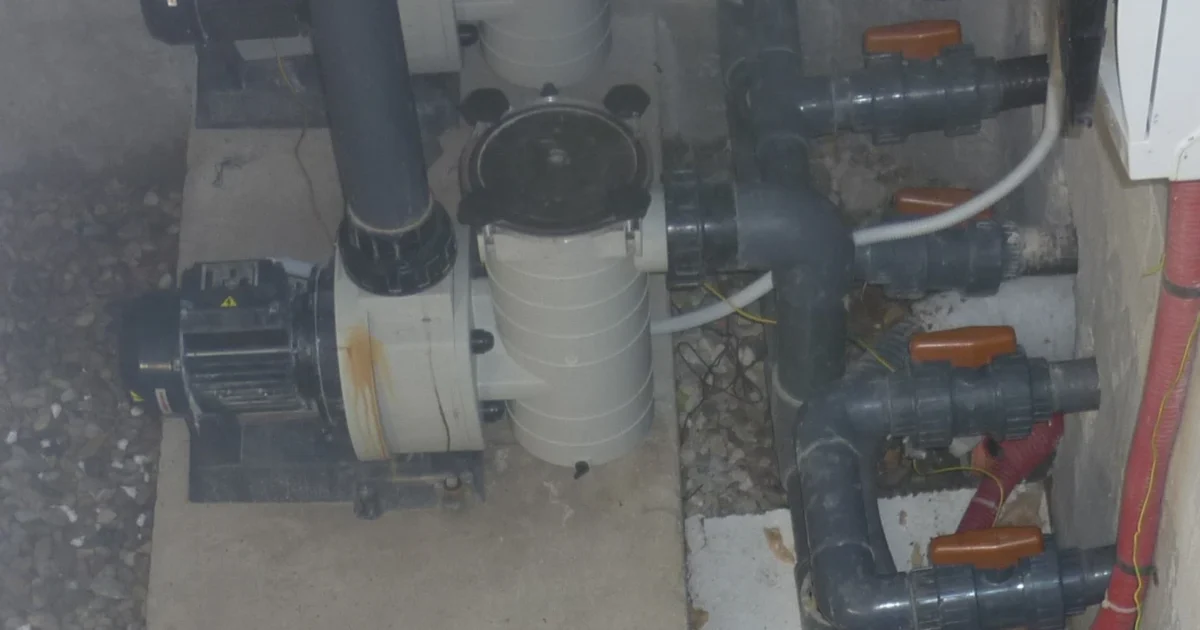 Pool pump motor, strainer housing and connected pipework at a swimming pool.