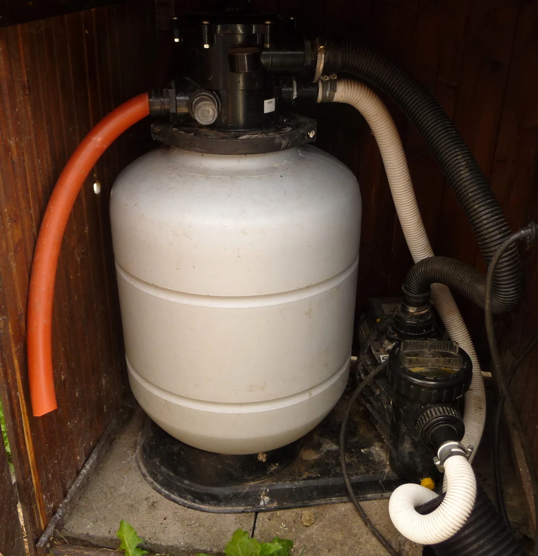A small pool pump beside a larger sand filter, joined by hoses.