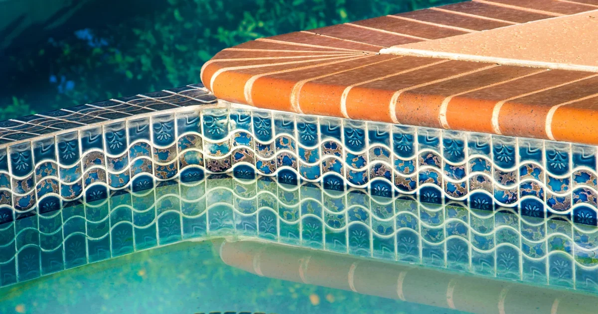 Decorative blue waterline tile beneath rounded brick coping at a pool edge.