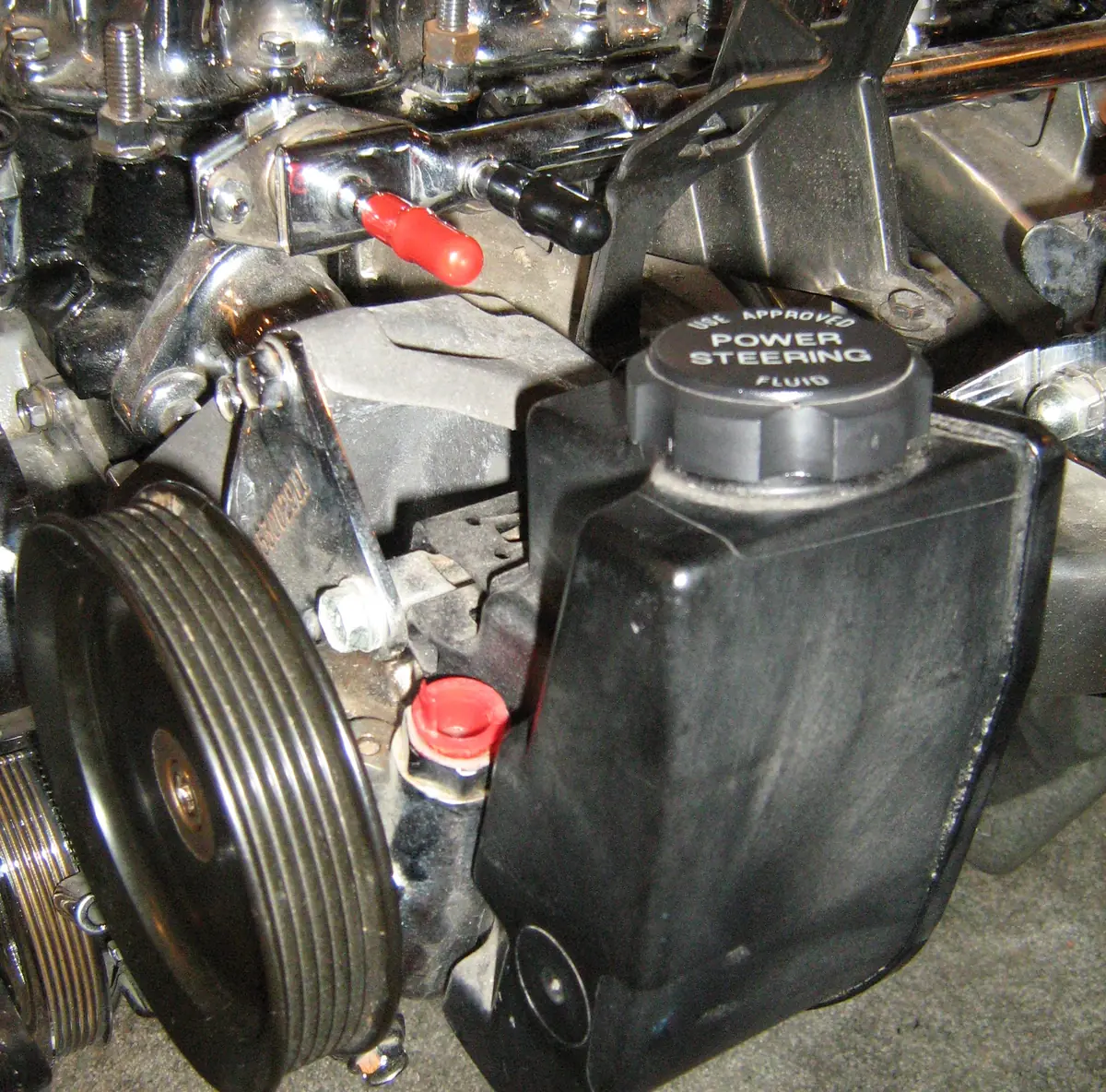 A chrome engine with a grooved pulley and a black reservoir whose cap reads power steering