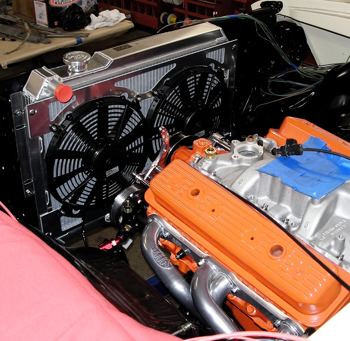 An aluminum radiator with two black electric fans beside an engine.