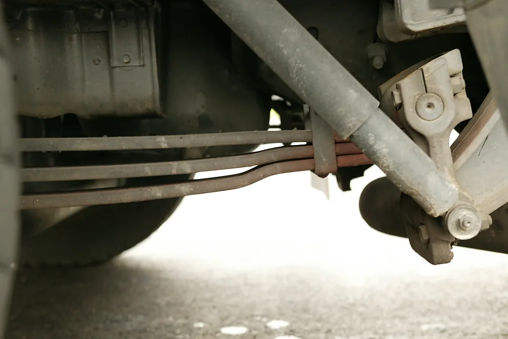 A long grey shock absorber running at an angle across the picture, bolted at its lower end next to a leaf spring