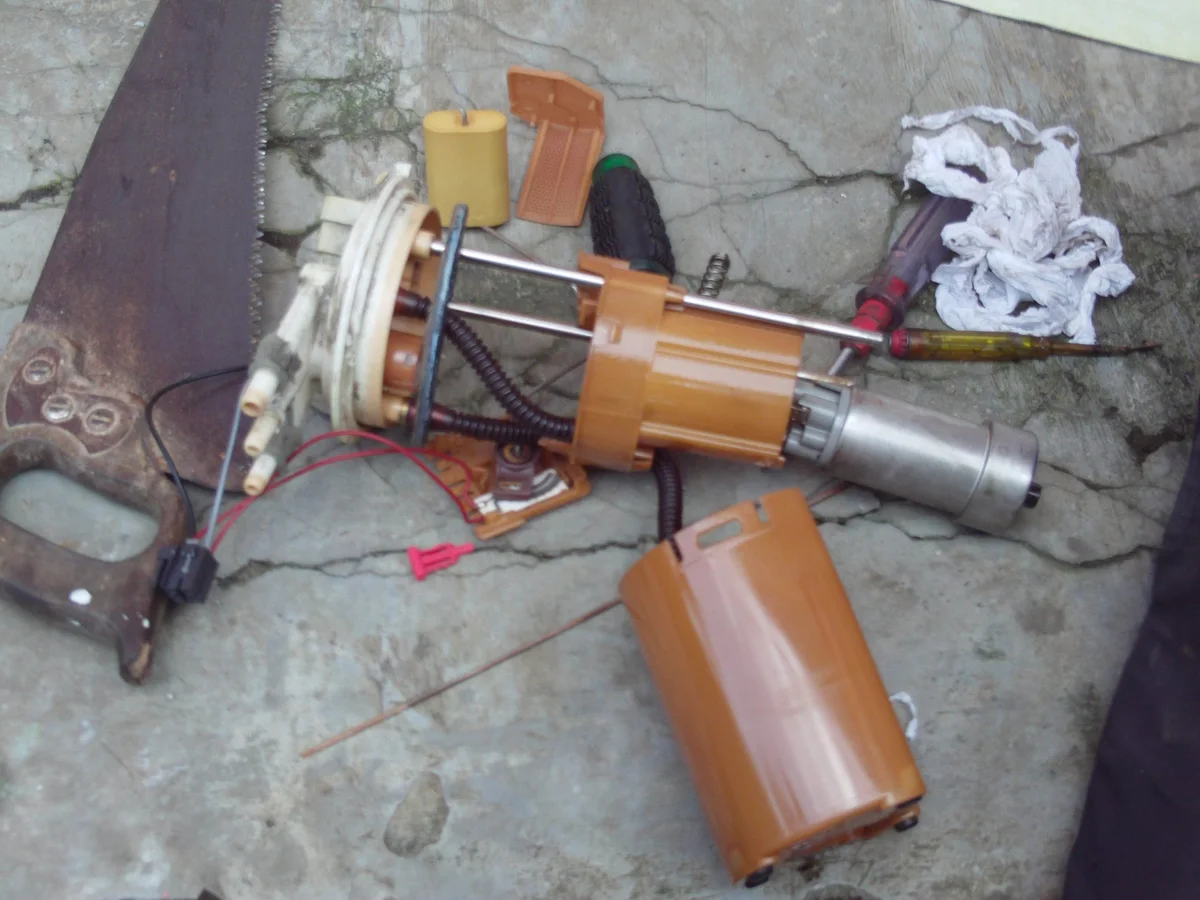 A removed fuel pump assembly with its mounting plate, tubes, pump and float.