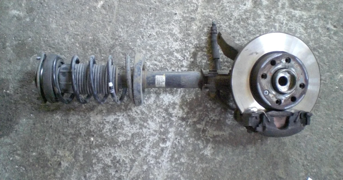 A removed front suspension assembly with coil spring, strut and wheel hub lying on the ground.