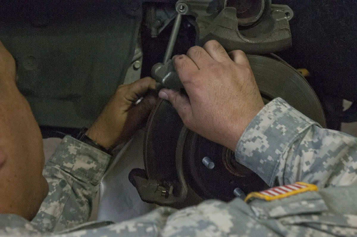 A man in uniform leans into a wheel well and cleans the brake rotor while the caliper is off during a brake pad job