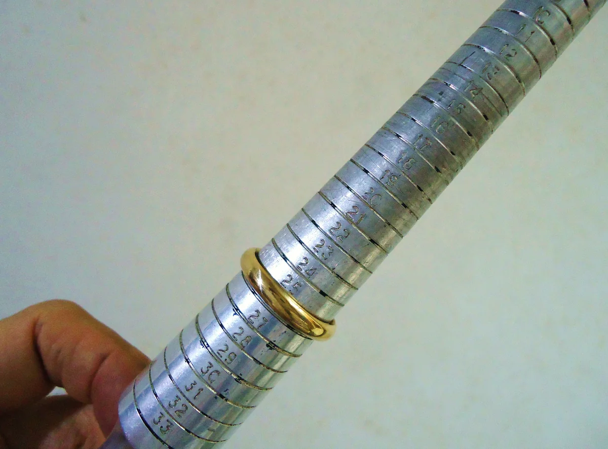 A jeweler holding a gold wedding band on a metal measuring mandrel.