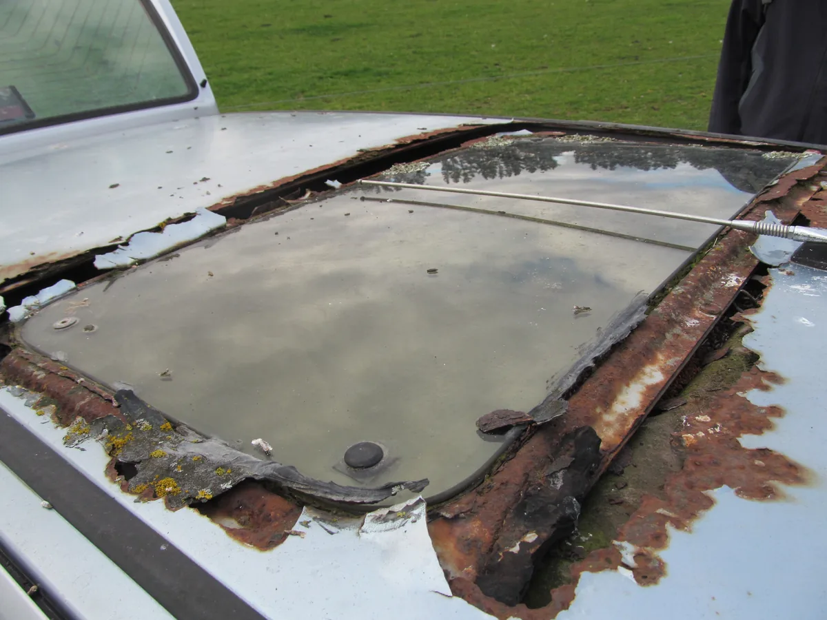 The roof of an old car with heavy rust around the edges of its sunroof opening