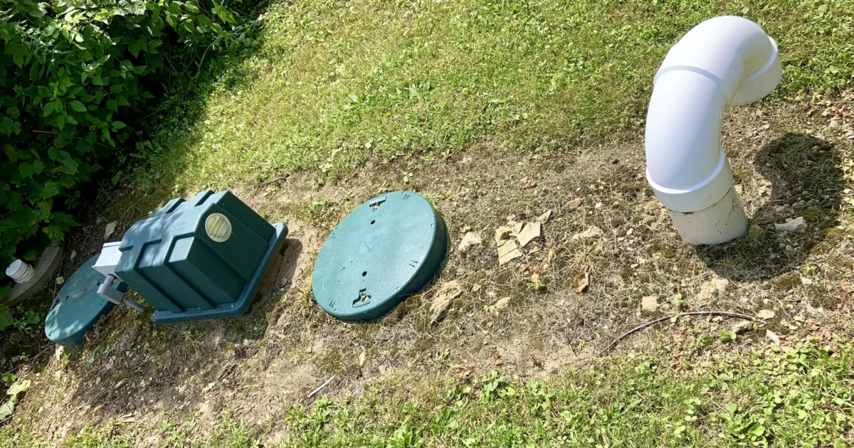 Green septic access covers and a white pipe at ground level beside a lawn.
