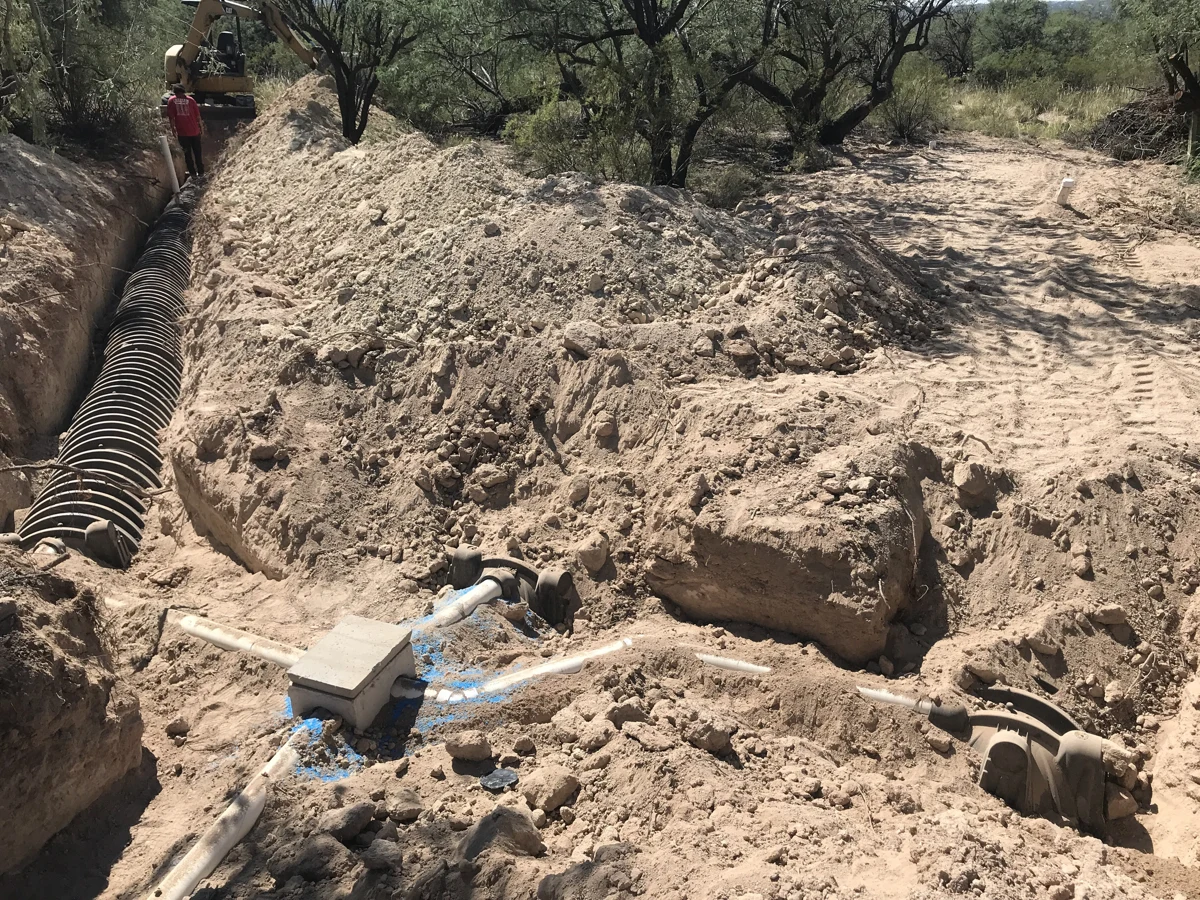 Open soil trenches with a distribution box and black chamber sections of a septic drain field.
