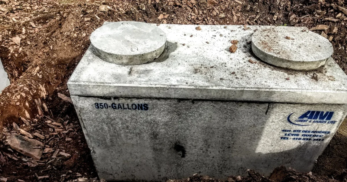 Concrete septic tank with two round access lids sitting in an excavated hole.
