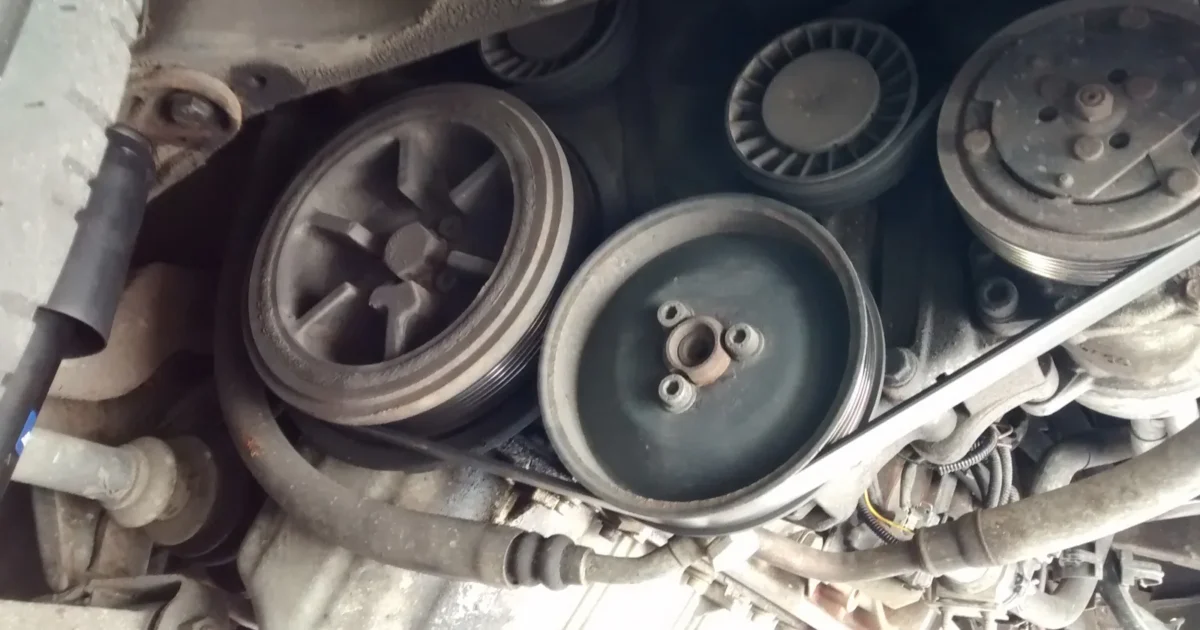 The front of an engine with several round pulleys and a ribbed belt running around them