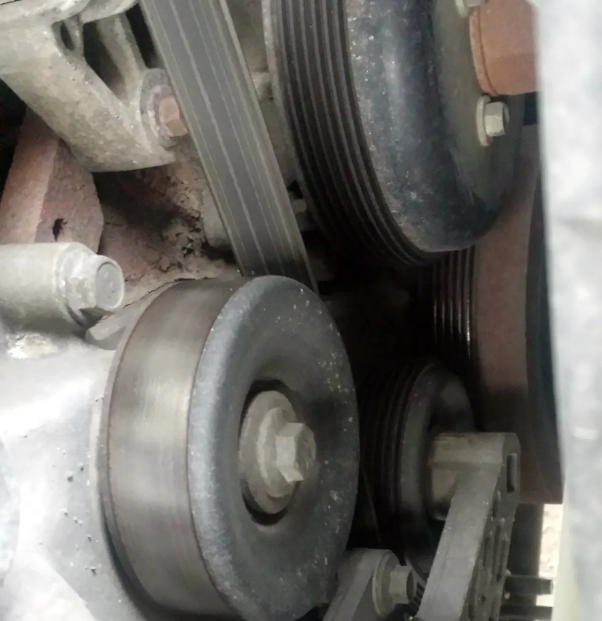 Close up of a smooth metal pulley on a spring loaded arm pressing on a ribbed engine belt