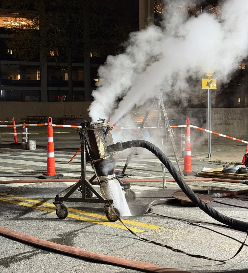 Steam and hoses at a sewer lining project on a street in Cambridge, Massachusetts.