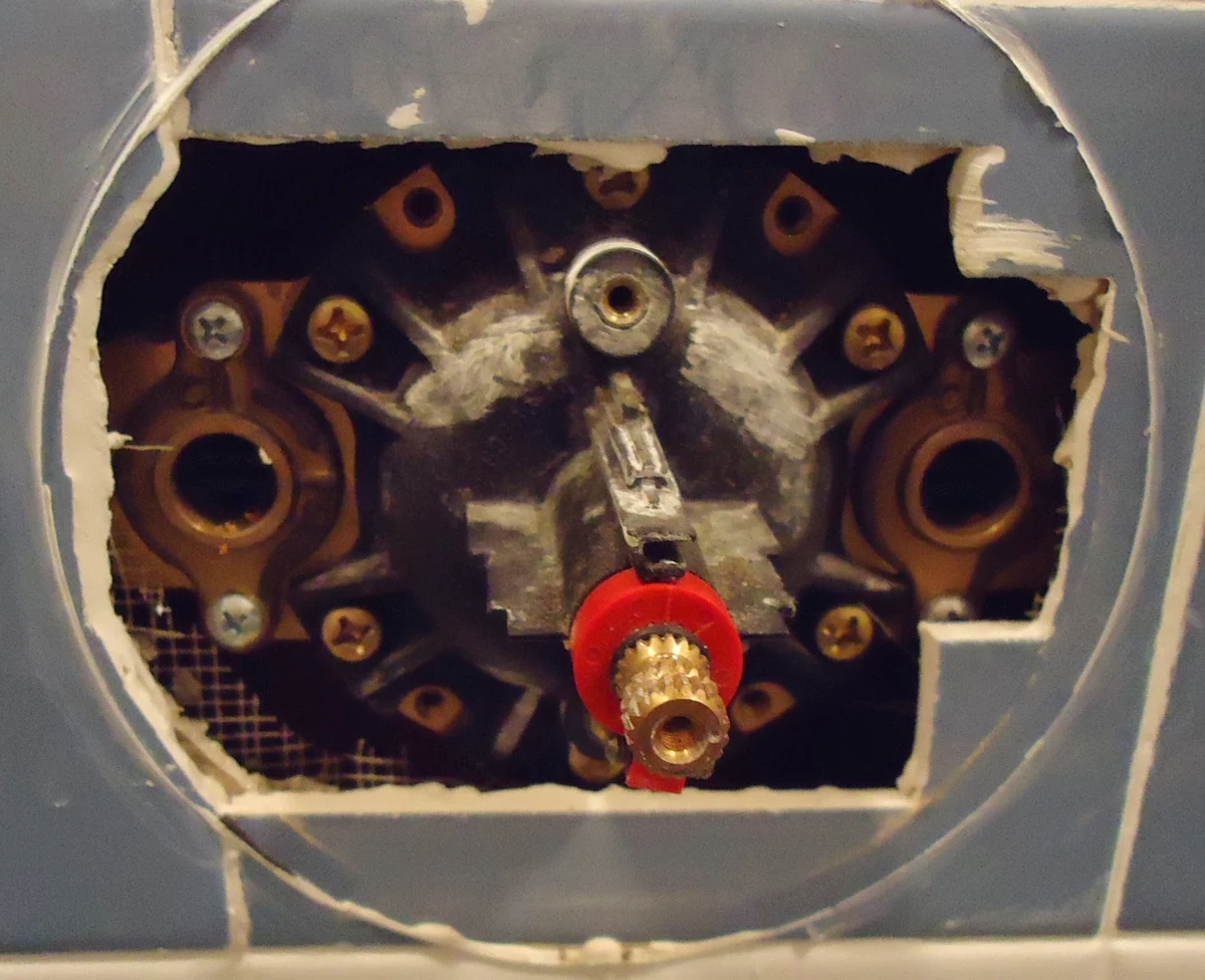 Tile cut away around a shower valve, exposing its connections.