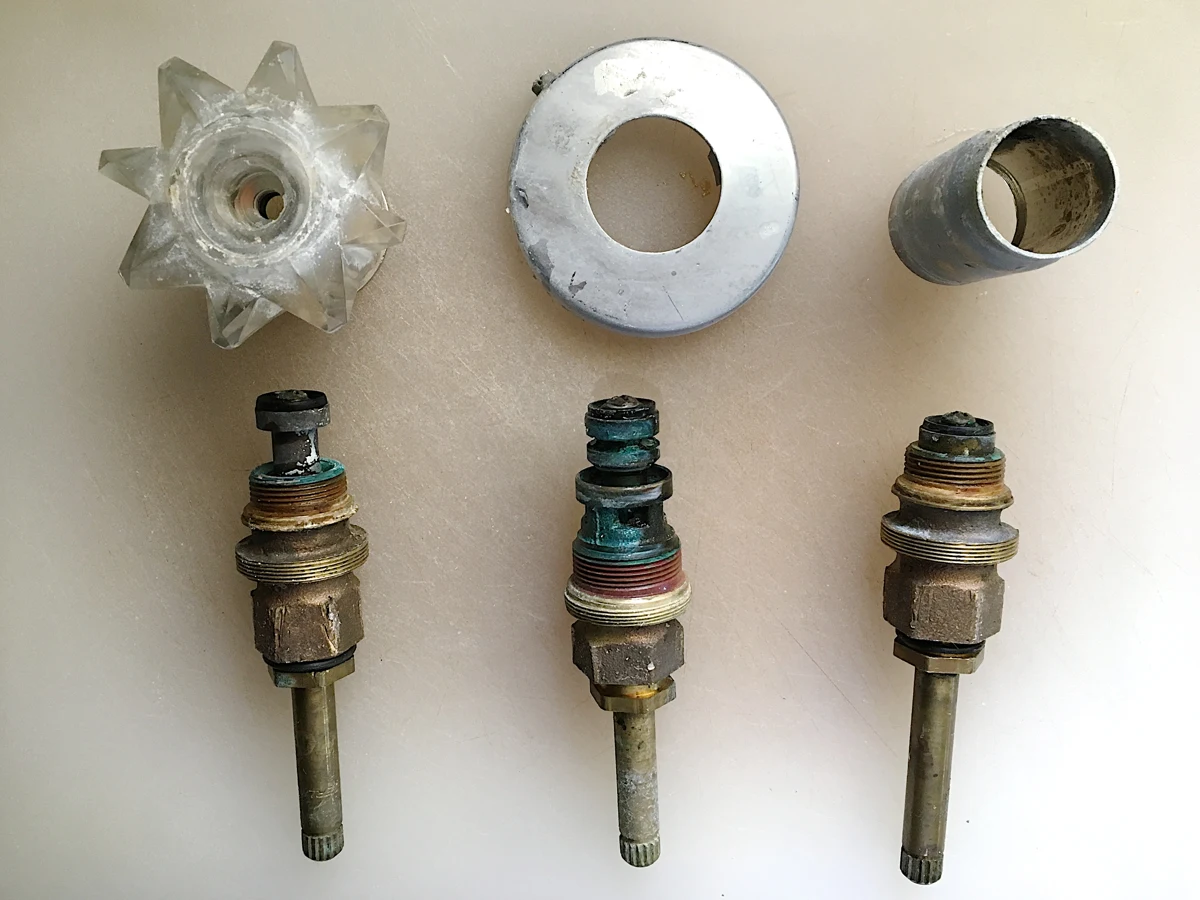 Three removed valve stems beneath the handle and trim pieces.