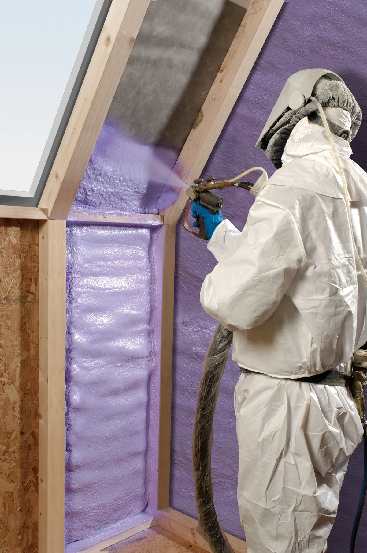 A specialist contractor spraying purple polyurethane foam onto interior framing.