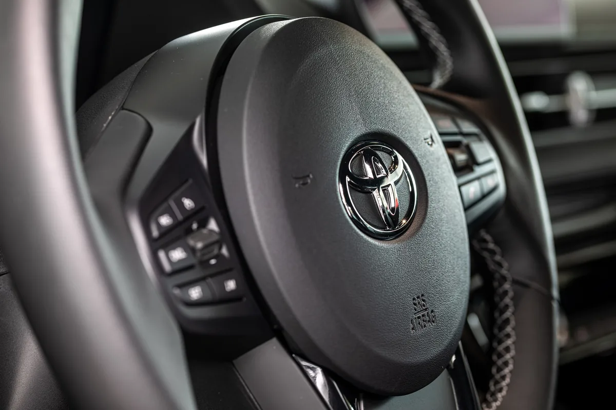 The steering wheel of a Toyota GR Supra with the airbag cover in the middle and control buttons on the spokes