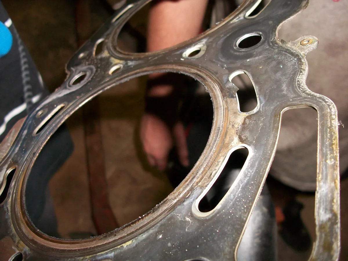Close up of a metal head gasket around one cylinder opening, with a worn, dark edge