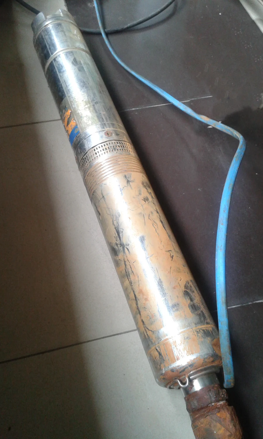 Long cylindrical stainless submersible pump with its cable, removed from the well.