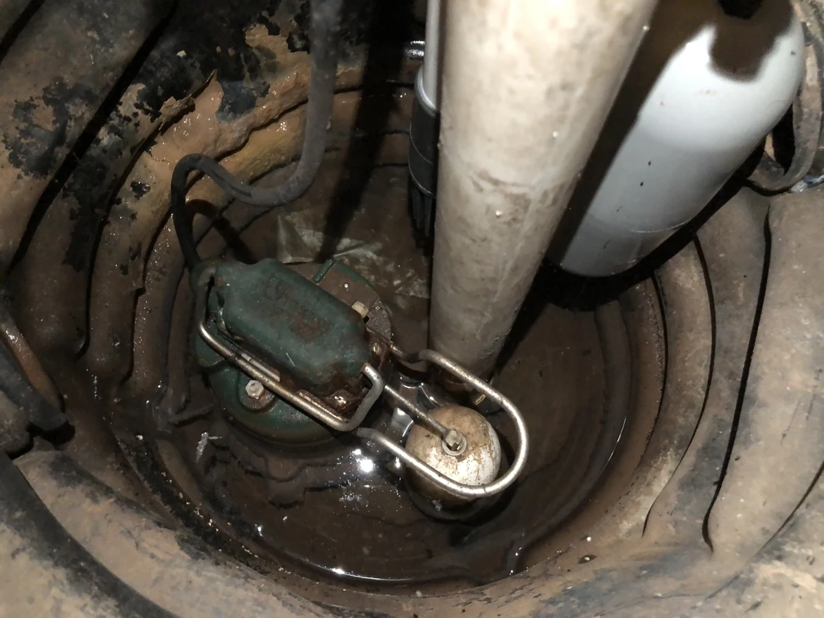 Sump pump and white discharge pipe inside a round basement pit.