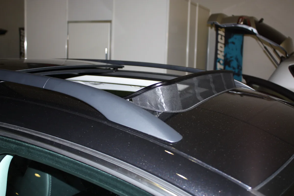 An open sunroof on a dark car roof with a clear wind deflector raised at its front edge