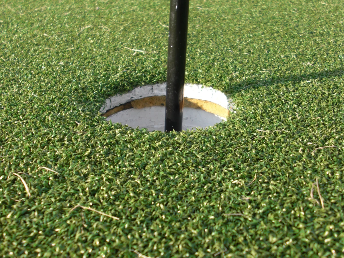 Close view of a golf cup and flagpole in an artificial-turf putting green.