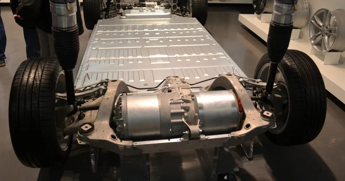 The bare base of a Tesla Model S on display, with the flat silver battery pack filling the floor between the wheels